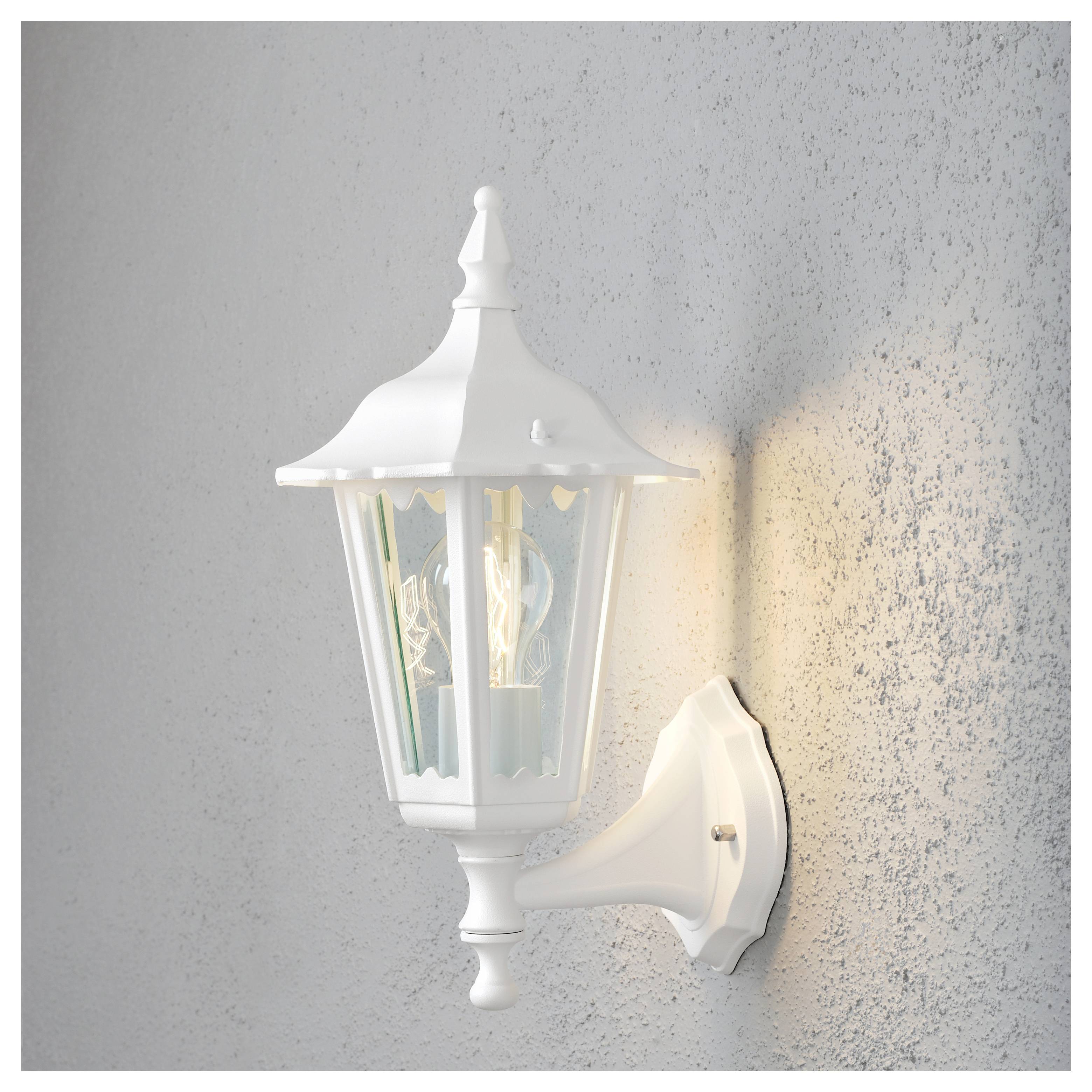 Eine weiße Außenwandlaterne mit klassischem Design, an einer strukturierten Wand montiert, leuchtet sanft und wirft einen dezenten Schein.