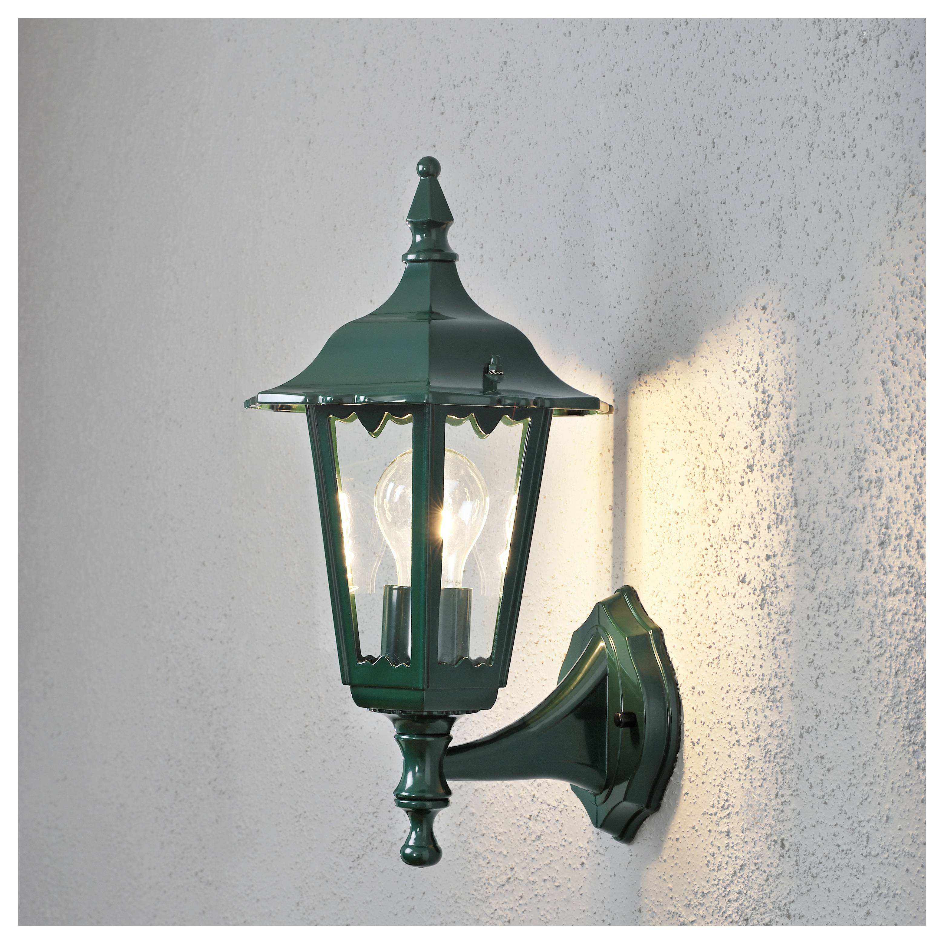 Grüne, wandmontierte Laterne mit einer leuchtenden Glühbirne, die Licht auf eine strukturierte Wand wirft; klassisches Design mit dekorativem Abschlussknauf.