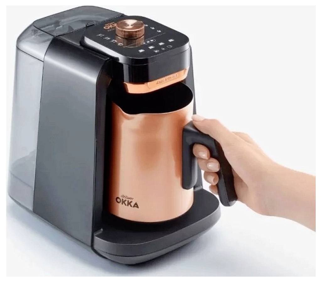 Eine Hand platziert einen kupferfarbenen Topf in eine kompakte Kaffeemaschine mit der Bezeichnung 