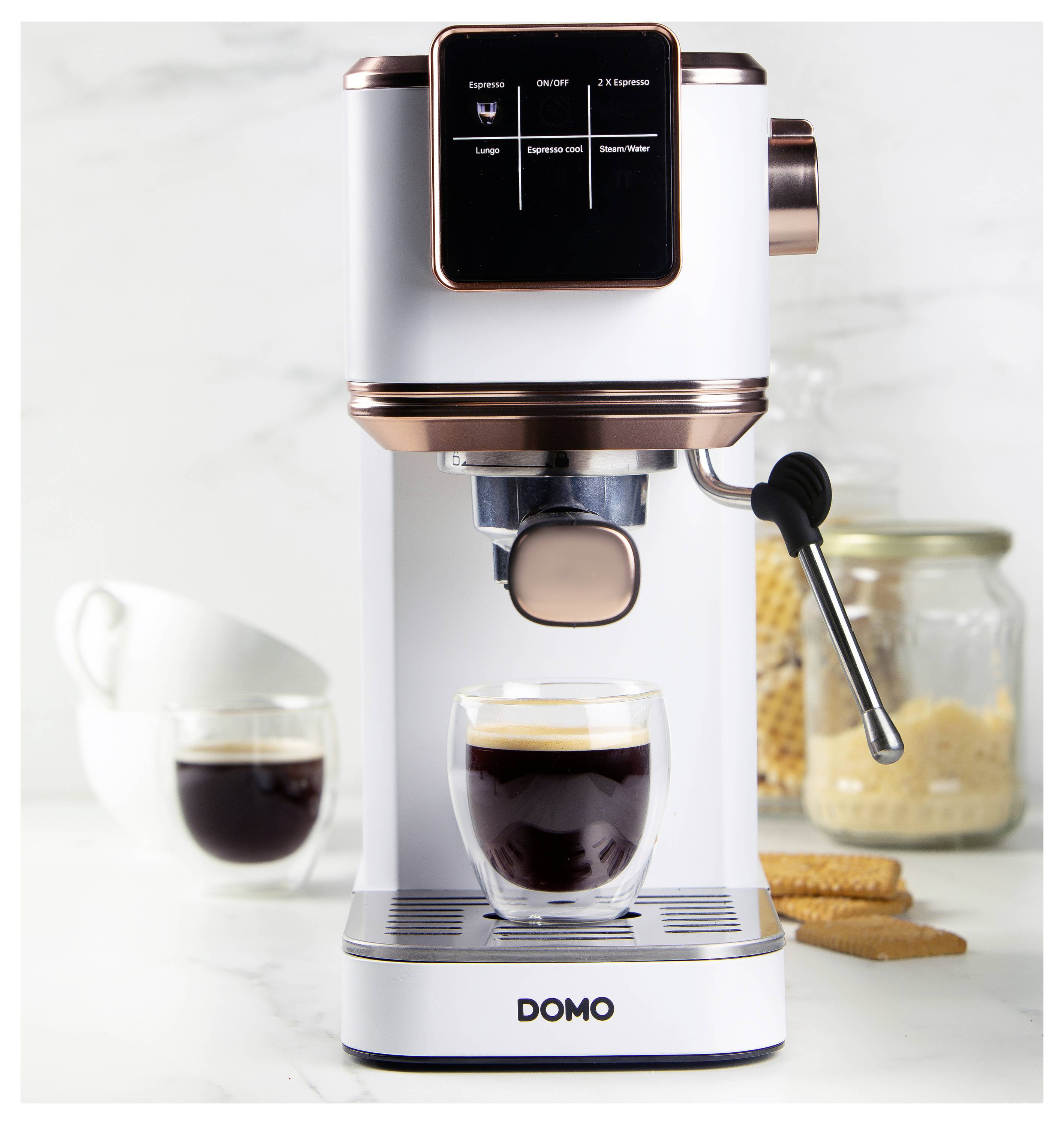 Espressomaschine, die Kaffee in eine Glastasse braut, mit einem angeschlossenen Milchaufschäumer. Tassen und Keksdose im Hintergrund.