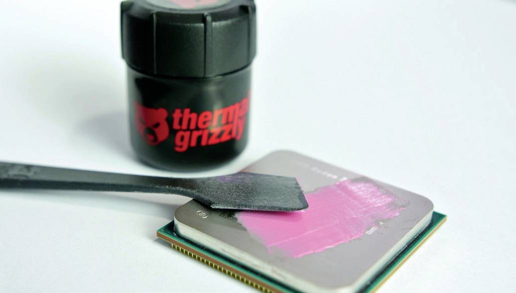 Auftragen von Wärmeleitpaste aus einem 'Thermal Grizzly' Behälter auf einen Computerprozessor mit einem Spatel.