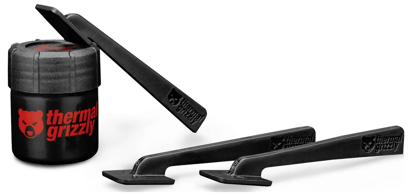 Ein kleiner schwarzer Behälter mit dem 'Thermal Grizzly' Logo liegt neben drei schwarzen Applikationswerkzeugen. Alle Gegenstände befinden sich auf einem weißen Hintergrund.