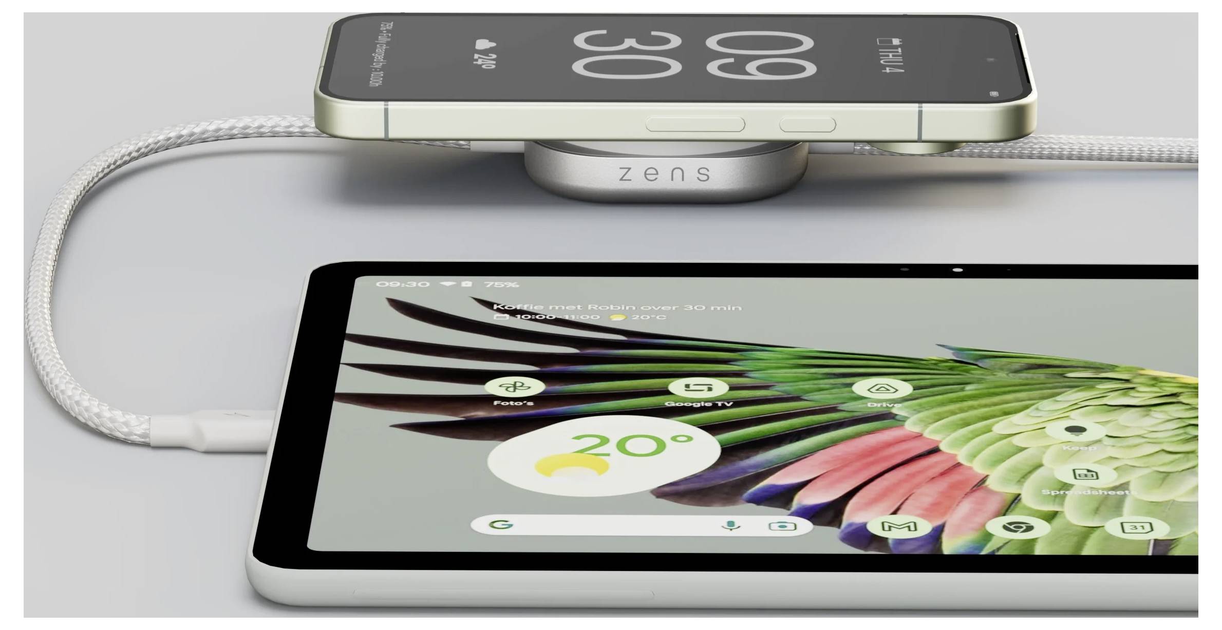 Ein Smartphone wird drahtlos auf einem Zens-Ladegerät geladen, das neben einem Tablet steht, auf dem ein bunter Papagei und ein Wetterwidget mit 20°C zu sehen sind.