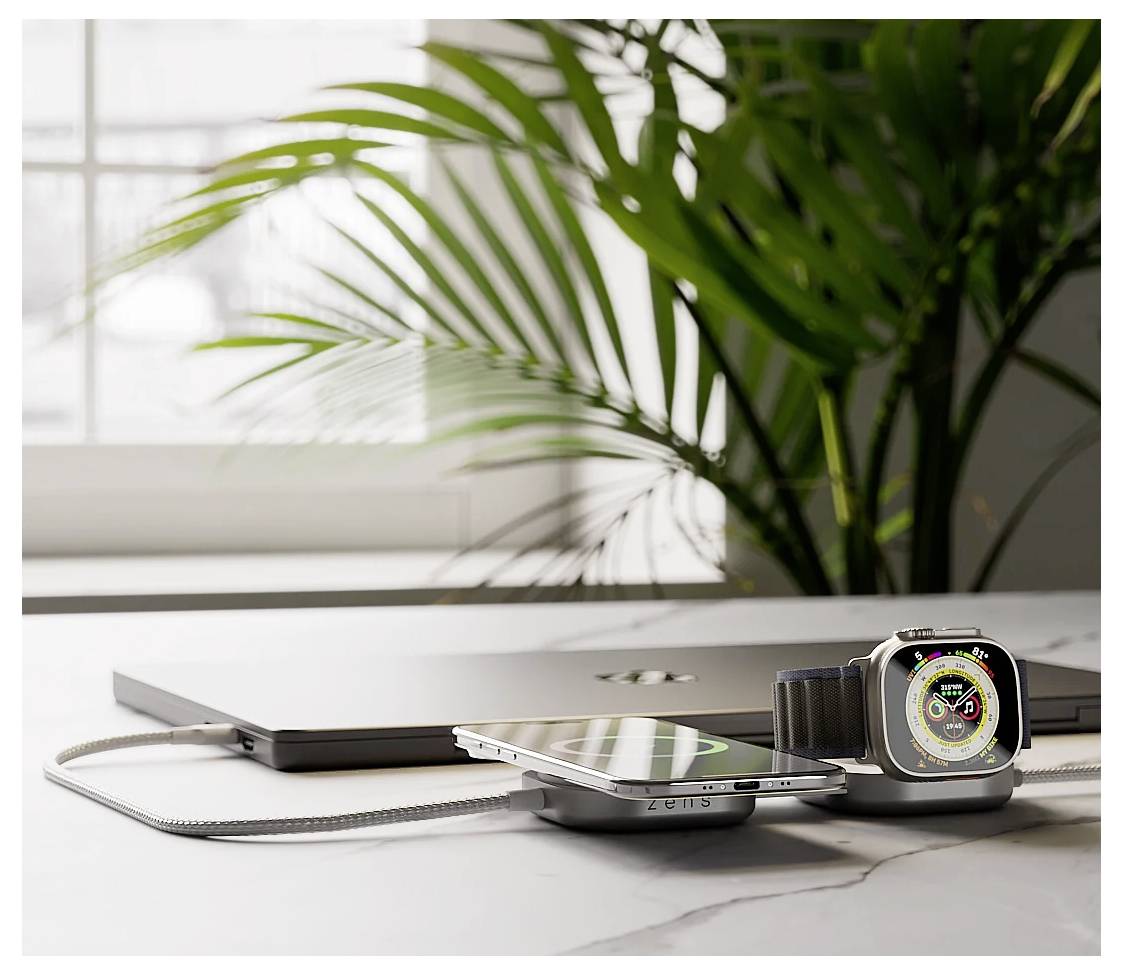 Ein Smartphone und eine Smartwatch, die auf einer dualen drahtlosen Ladestation platziert sind, die auf einem Marmortisch neben einem geschlossenen Laptop und einer großen Pflanze steht.