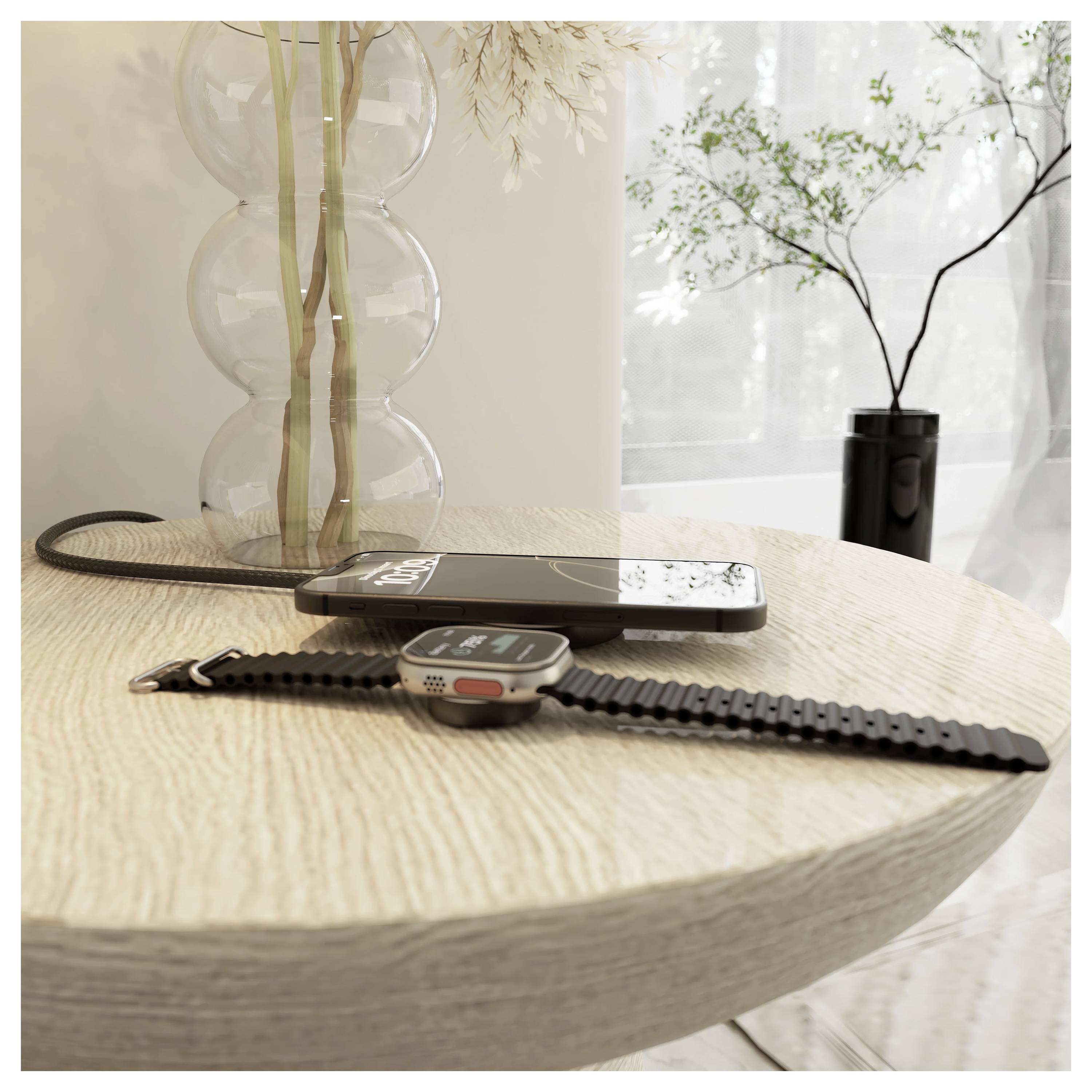 Eine Smartwatch mit einem schwarzen Armband und einem Ladekabel liegt auf einem runden Holztisch neben einer Zierpflanze und einem sonnendurchfluteten Fenster.