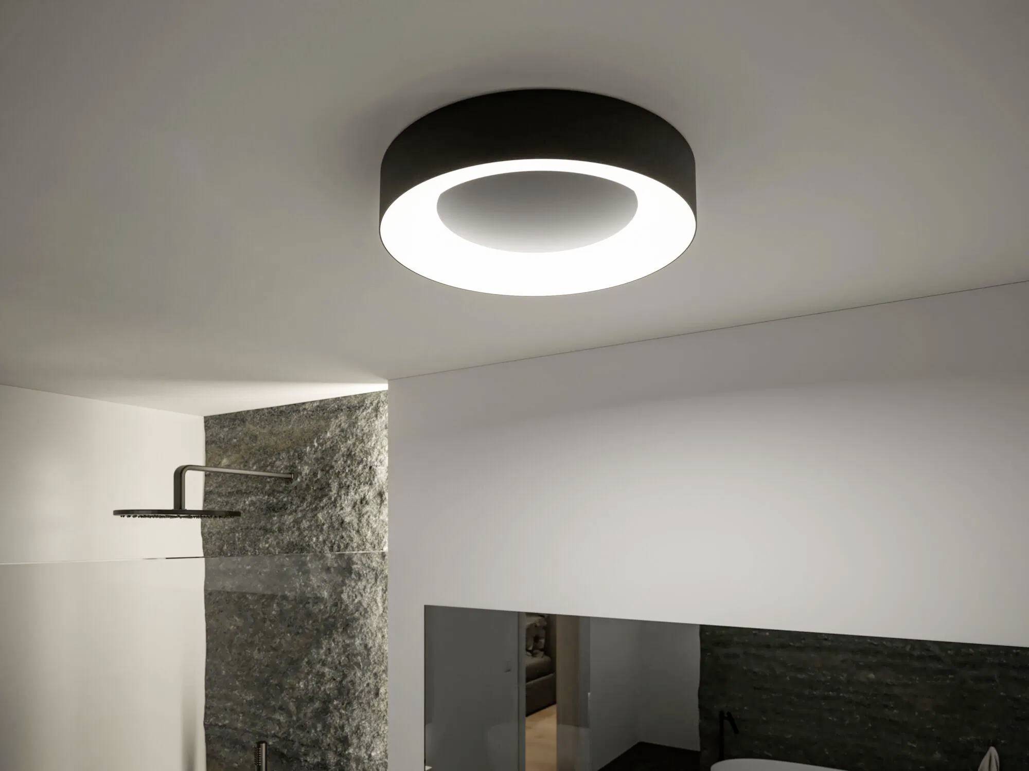 Moderne kreisförmige Deckenleuchte in einem minimalistischen Raum, die eine strukturierte Wand und einen Glasduschbereich darunter beleuchtet.
