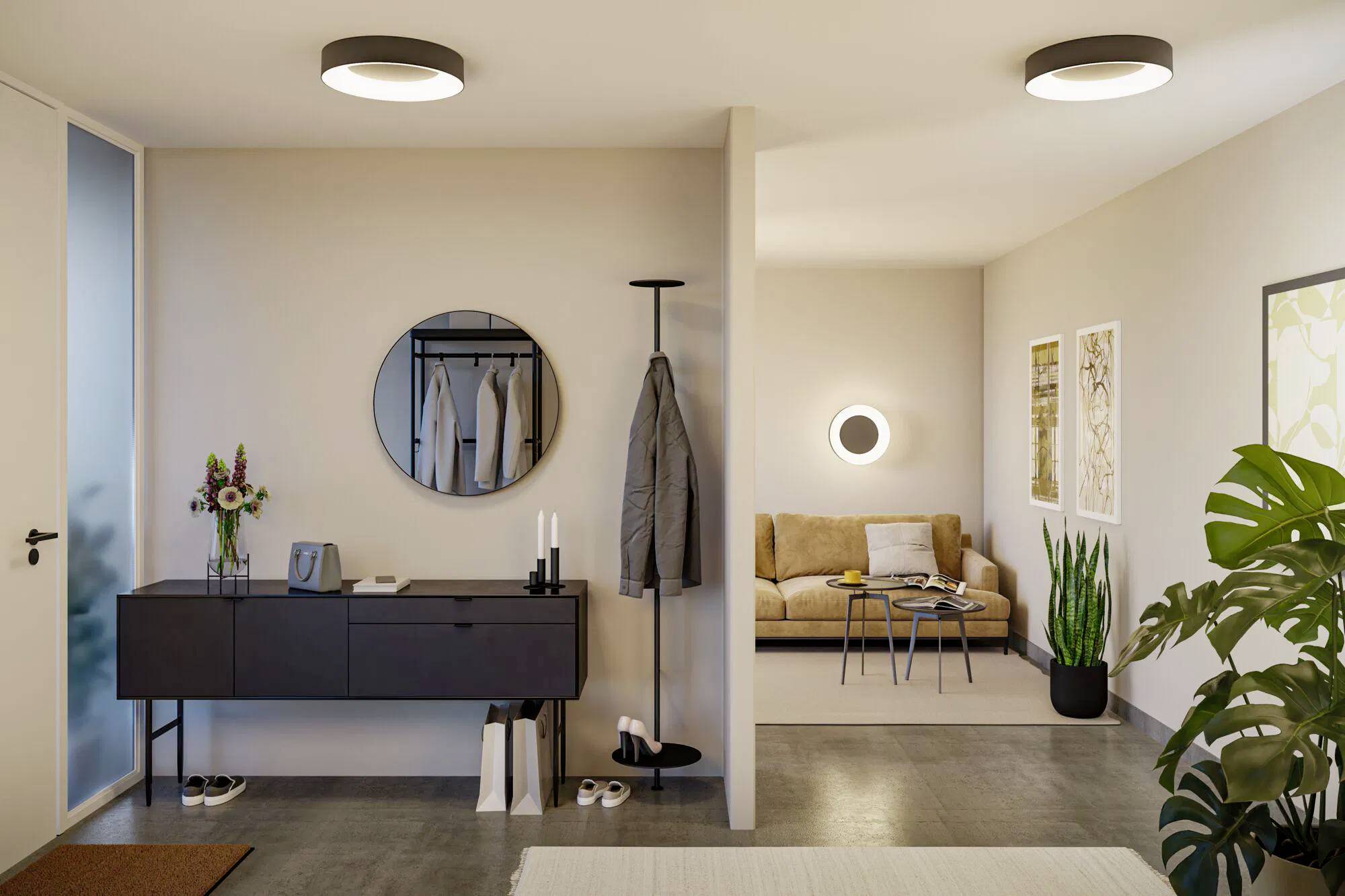 Eine moderne, minimalistische Wohnungsdiele mit einem runden Spiegel, einer Garderobe und einem Blick in das Wohnzimmer mit einer Couch und Pflanzen.