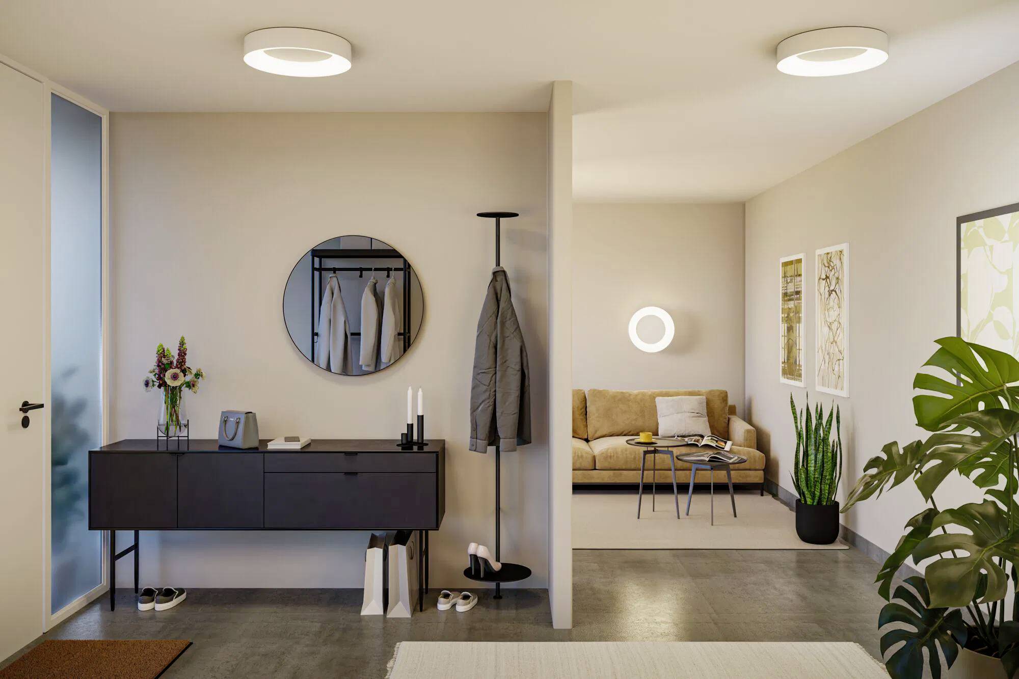 Moderne Wohnzimmer und Flur mit minimalistischer Einrichtung. Der Flur verfügt über eine dunkle Konsole, einen Spiegel und eine Garderobe. Der Wohnbereich hat ein beiges Sofa, Pflanzen und Wandkunst.