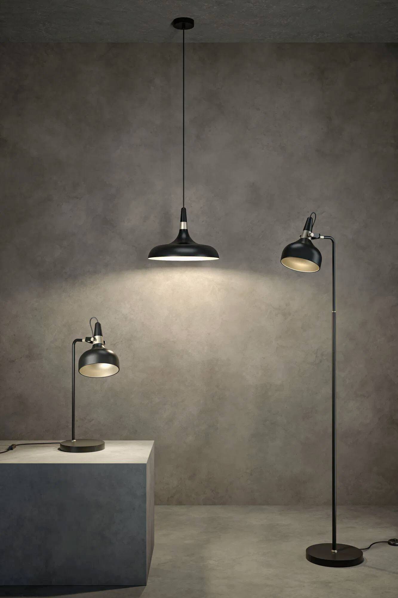 Drei schwarze Lampen beleuchten einen grauen Raum: ein Pendelleuchter von der Decke, eine Schreibtischlampe auf einem Tisch und eine hohe Stehlampe, die das Licht nach oben wirft.