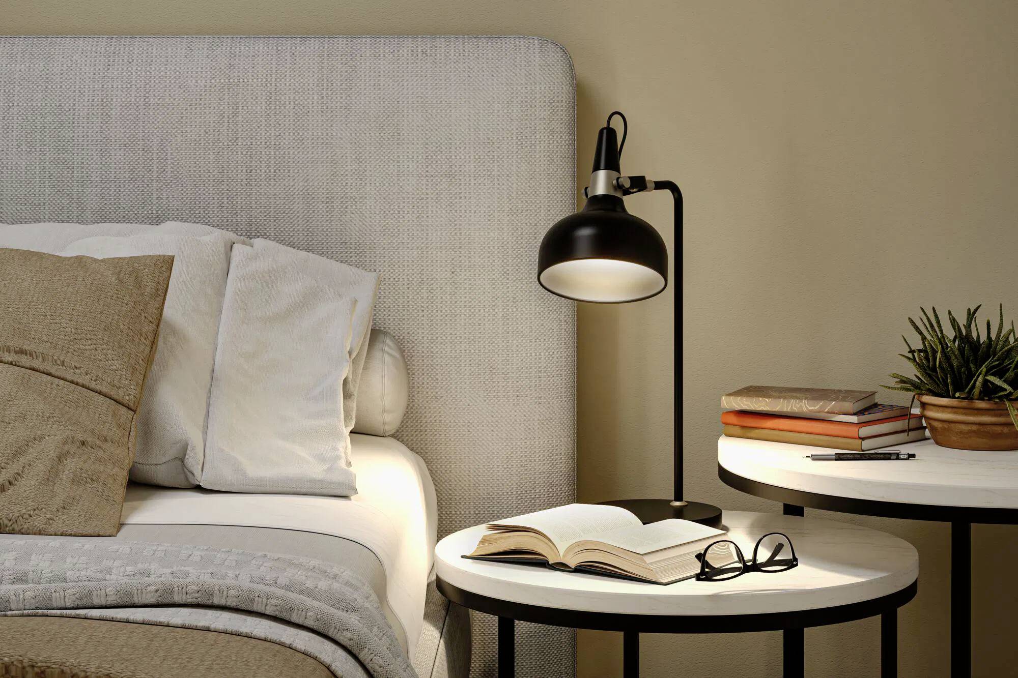 Ein gemütliches Schlafzimmer präsentiert ein Bett mit beigen Kissen, einen Nachttisch mit einem aufgeschlagenen Buch, Brille und einer modernen Lampe, was eine entspannende Atmosphäre schafft.