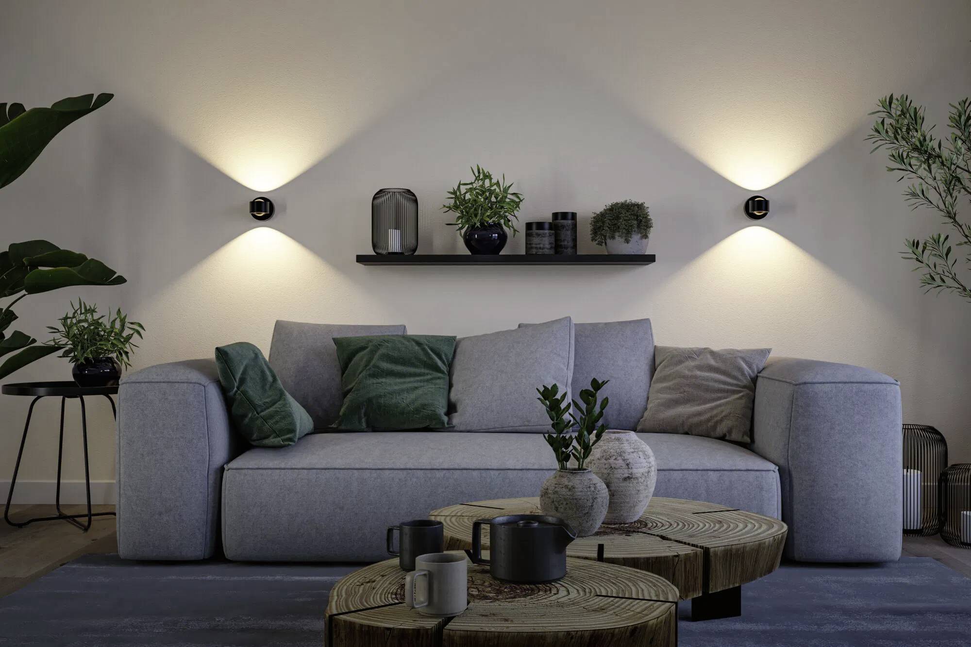 Ein modernes Wohnzimmer mit einem grauen Sofa, verschiedenen Topfpflanzen, einem Holzkaffeetisch und an der Wand montierten Leuchten, die gedämpftes Licht erzeugen.