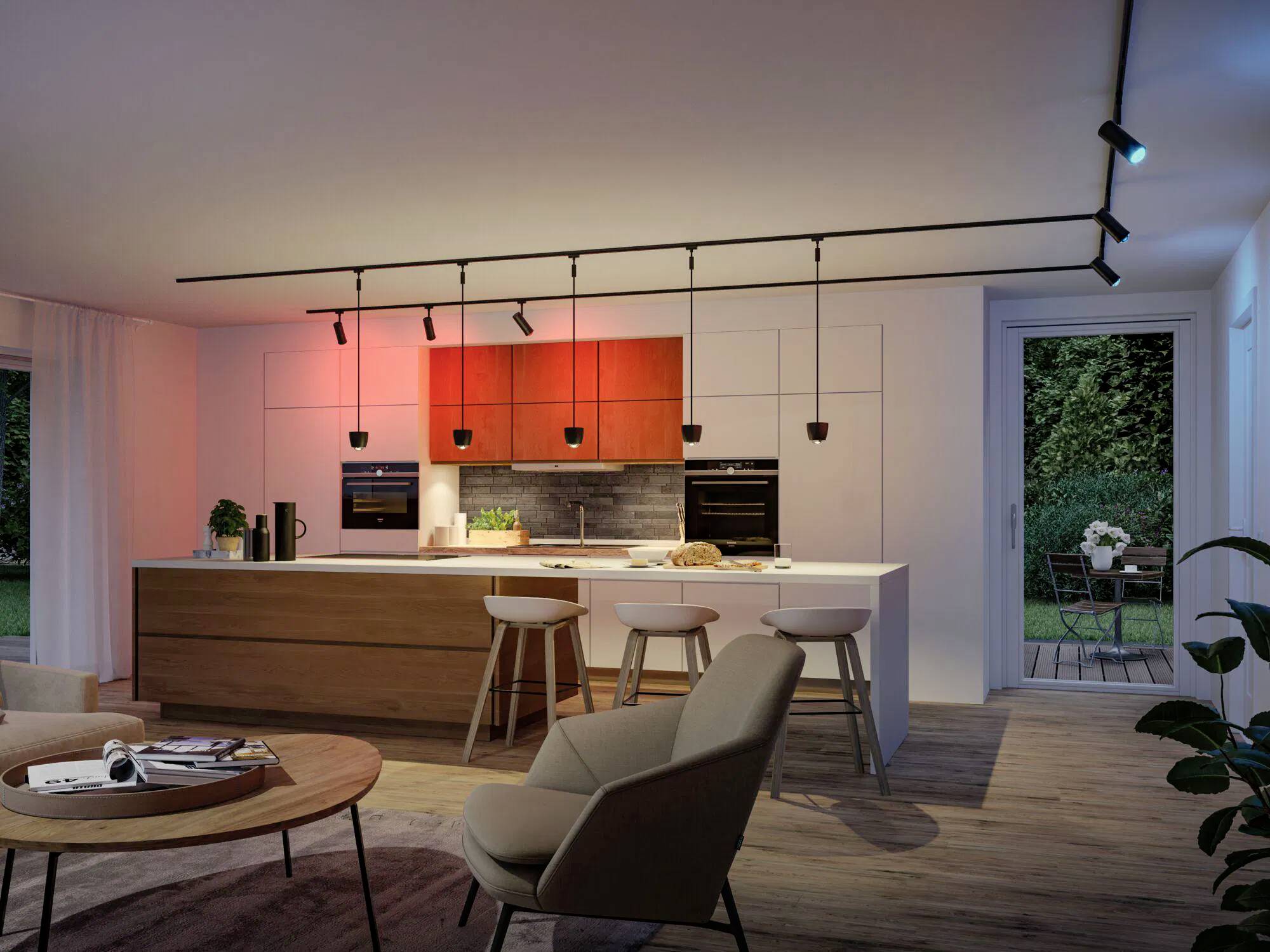Eine moderne Küche und ein Wohnbereich mit Schienenlicht und roten Akzenten. Beinhaltet eine Kochinsel, Barhocker und einen Blick in einen Garten durch Glastüren.