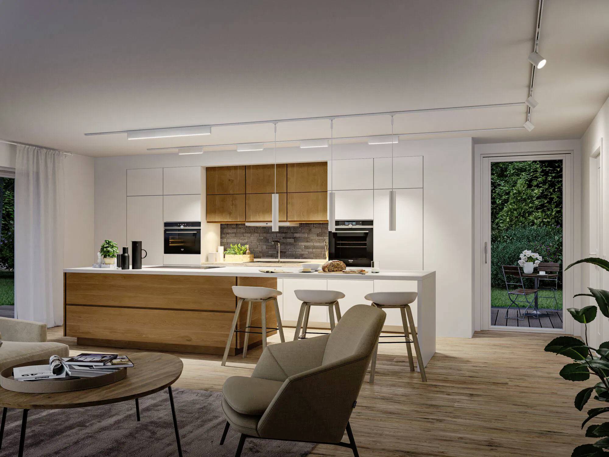 Moderne Küche und Wohnbereich mit hellen Holzschränken, Kücheninsel mit Barhockern, rundem Tisch, beigen Stühlen und großen Fenstern mit Blick auf einen Garten.