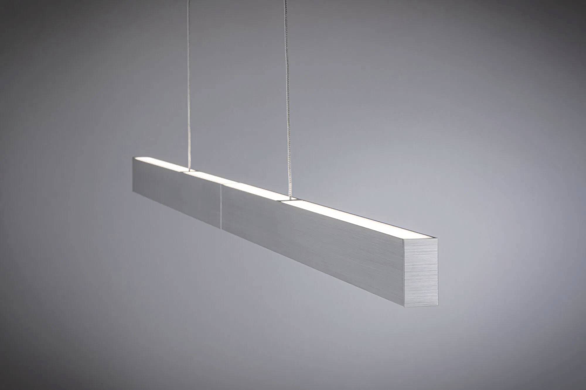 Eine moderne, rechteckige Pendelleuchte mit elegantem Design hängt vor einem schlichten grauen Hintergrund und verbreitet ein sanftes Leuchten.