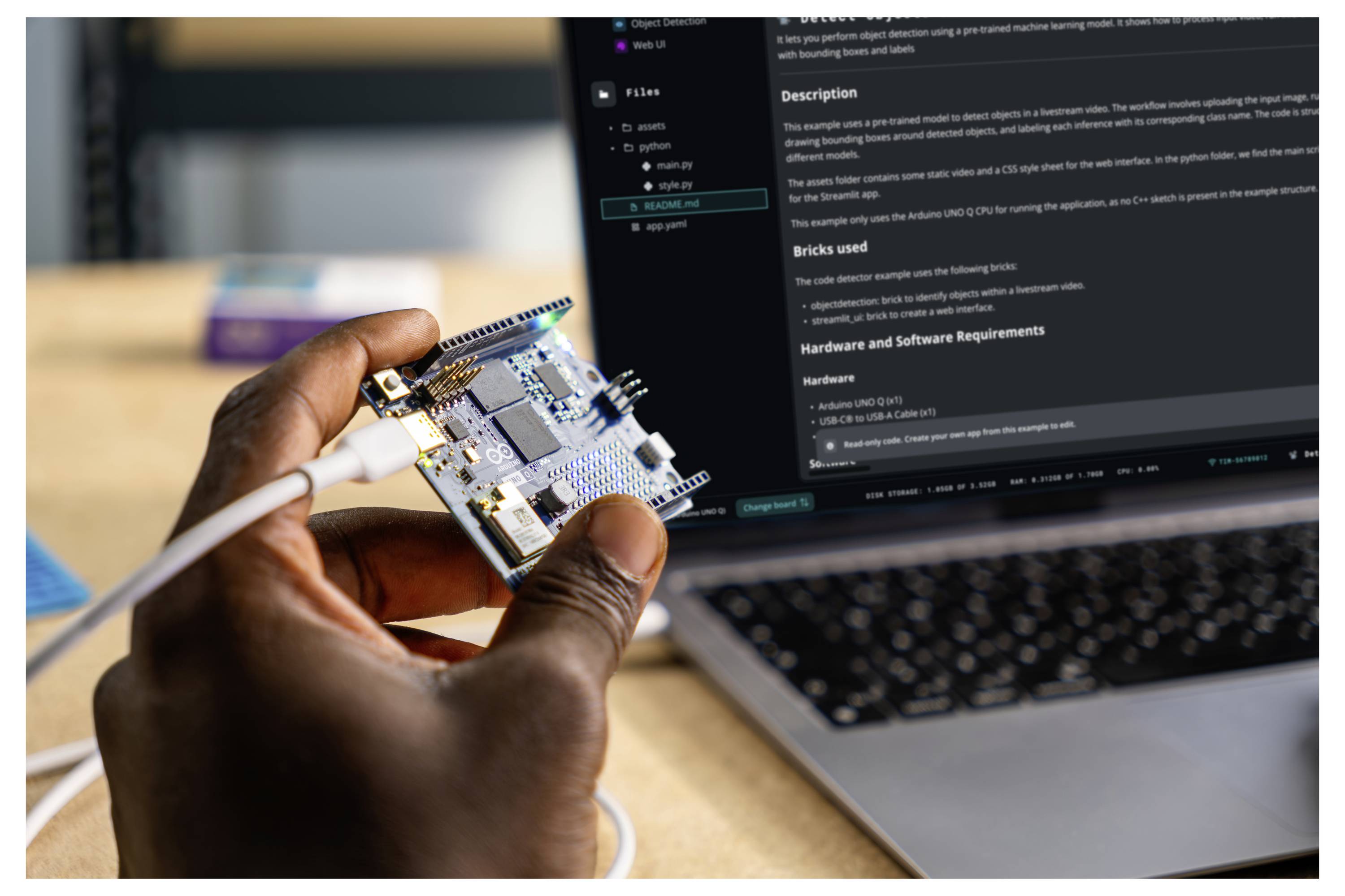Eine Person hält eine Mikrocontroller-Platine, die mit einem Kabel verbunden ist, vor einem Laptop, der Programmieranweisungen zeigt.
