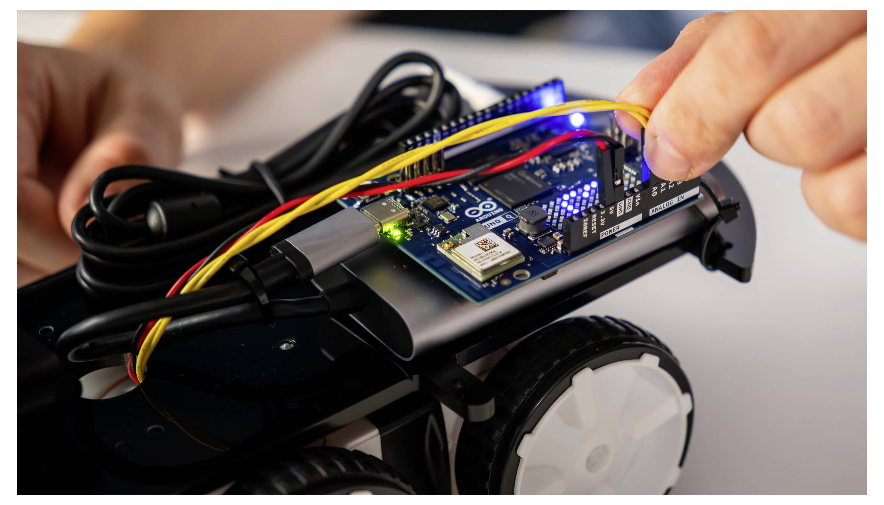 Eine Person baut ein kleines Roboterauto mit Leiterplatten und Kabeln zusammen.