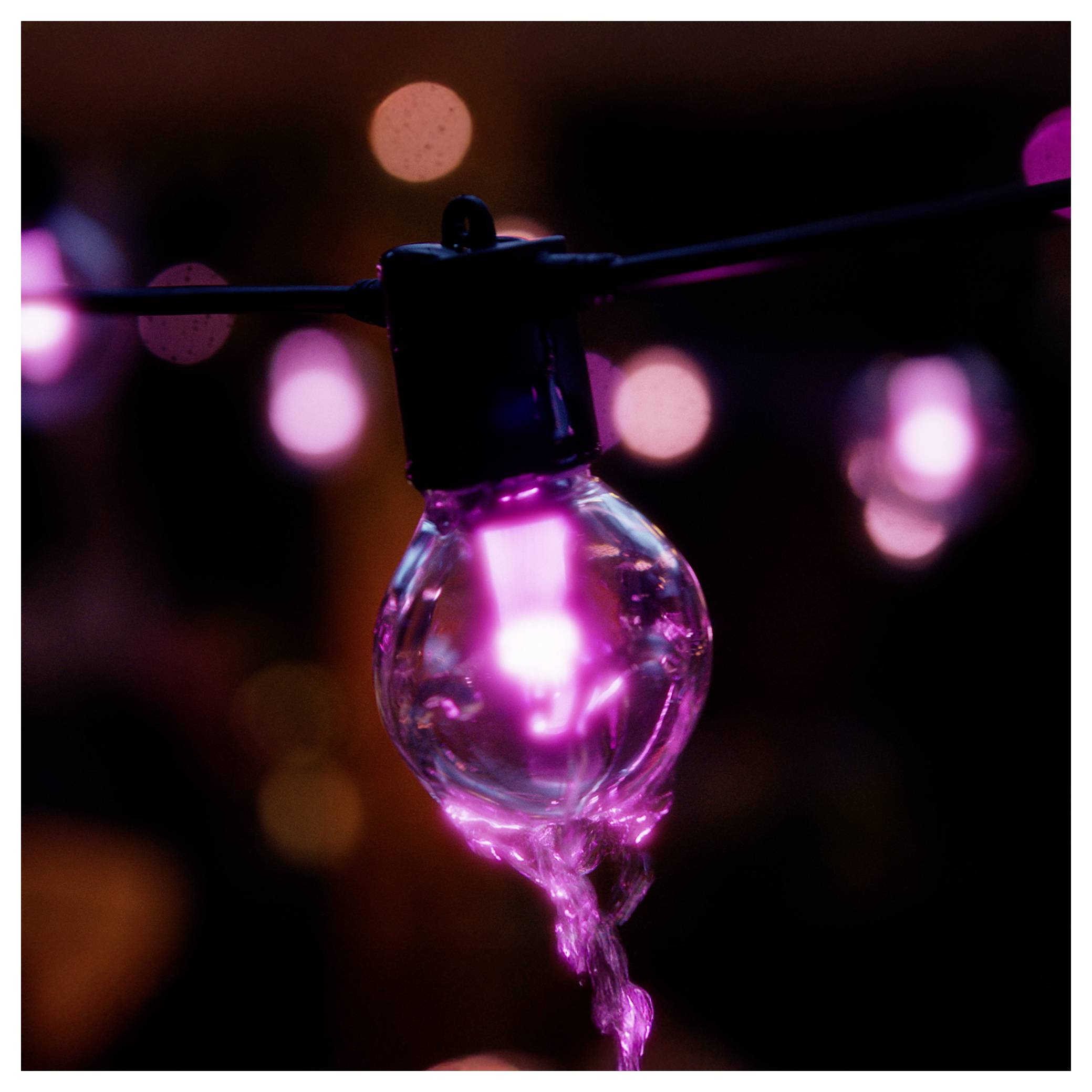 Eine Nahaufnahme einer leuchtend rosa Glühbirne, die an einem Draht hängt, mit verschwommenen rosa und orangefarbenen Lichtern im Hintergrund, die eine warme Atmosphäre erzeugen.
