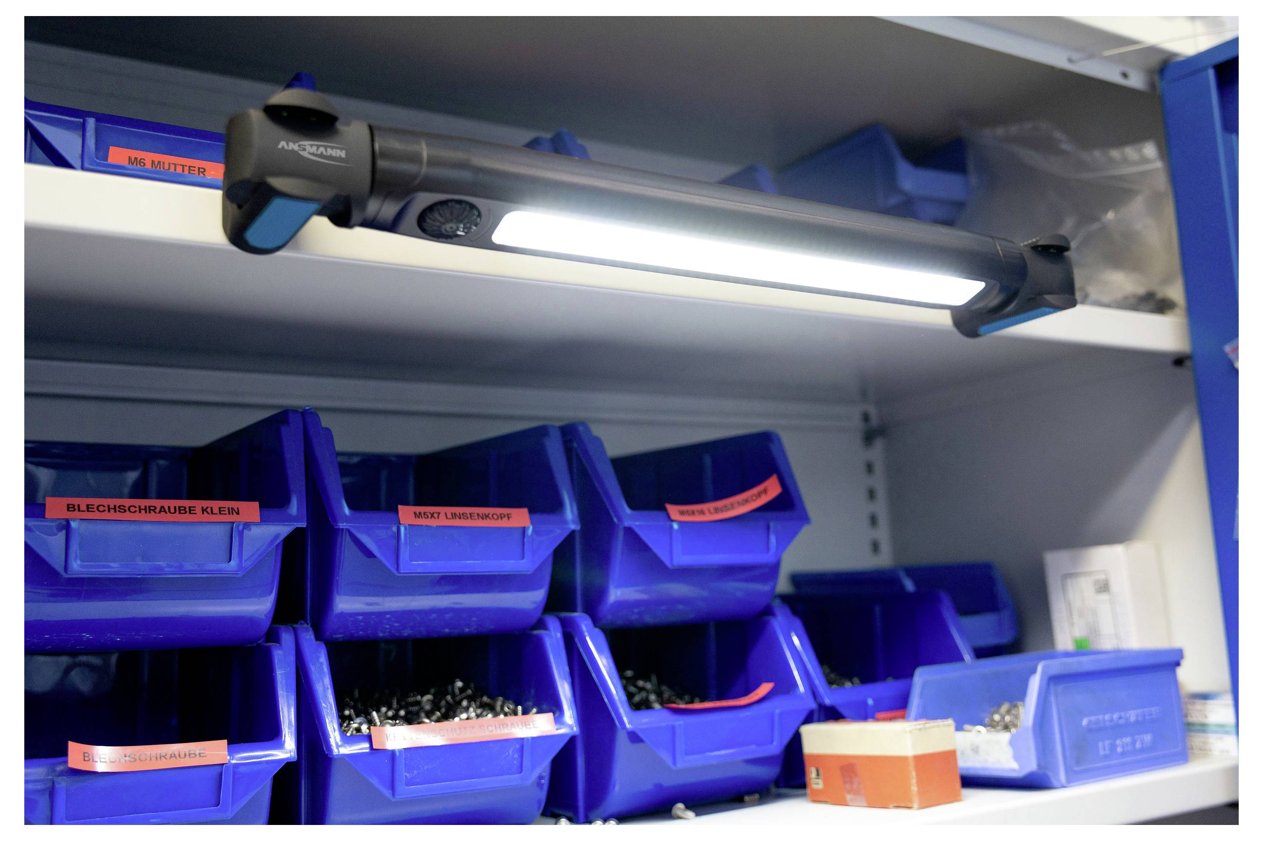 Eine beleuchtete LED-Arbeitsleuchte, die unter einem Regal befestigt ist und blaue Behälter mit verschiedenen Schrauben und Hardwarekomponenten auf den Regalen beleuchtet.