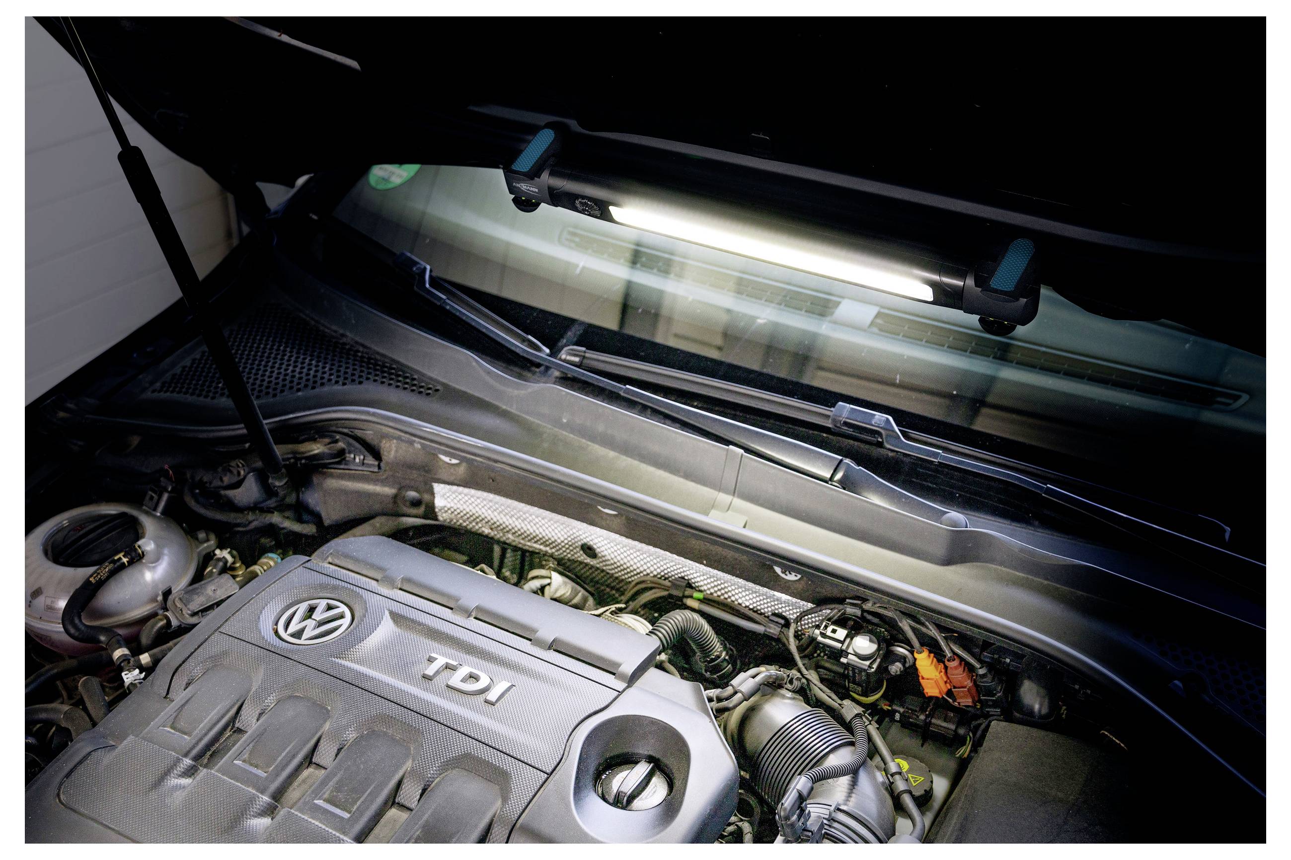 Motorraum eines Autos mit einem Volkswagen TDI-Motor, bei dem sichtbare Kabel und Komponenten unter einer geöffneten Motorhaube von Deckenlicht beleuchtet werden.