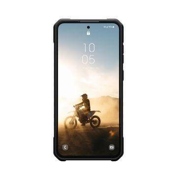 Ein robustes Smartphone zeigt einen Motorradfahrer auf staubigem Terrain bei Sonnenaufgang und unterstreicht Abenteuer und Widerstandsfähigkeit.