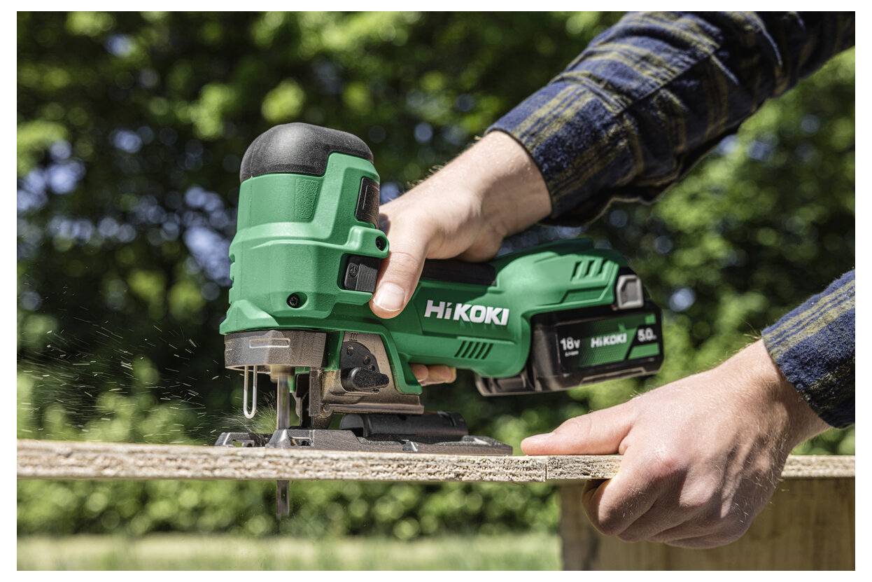 Eine Person, die ein grünes HiKOKI-Elektrowerkzeug verwendet, um eine Holzplatte im Freien, umgeben von Grünpflanzen, zu schneiden.