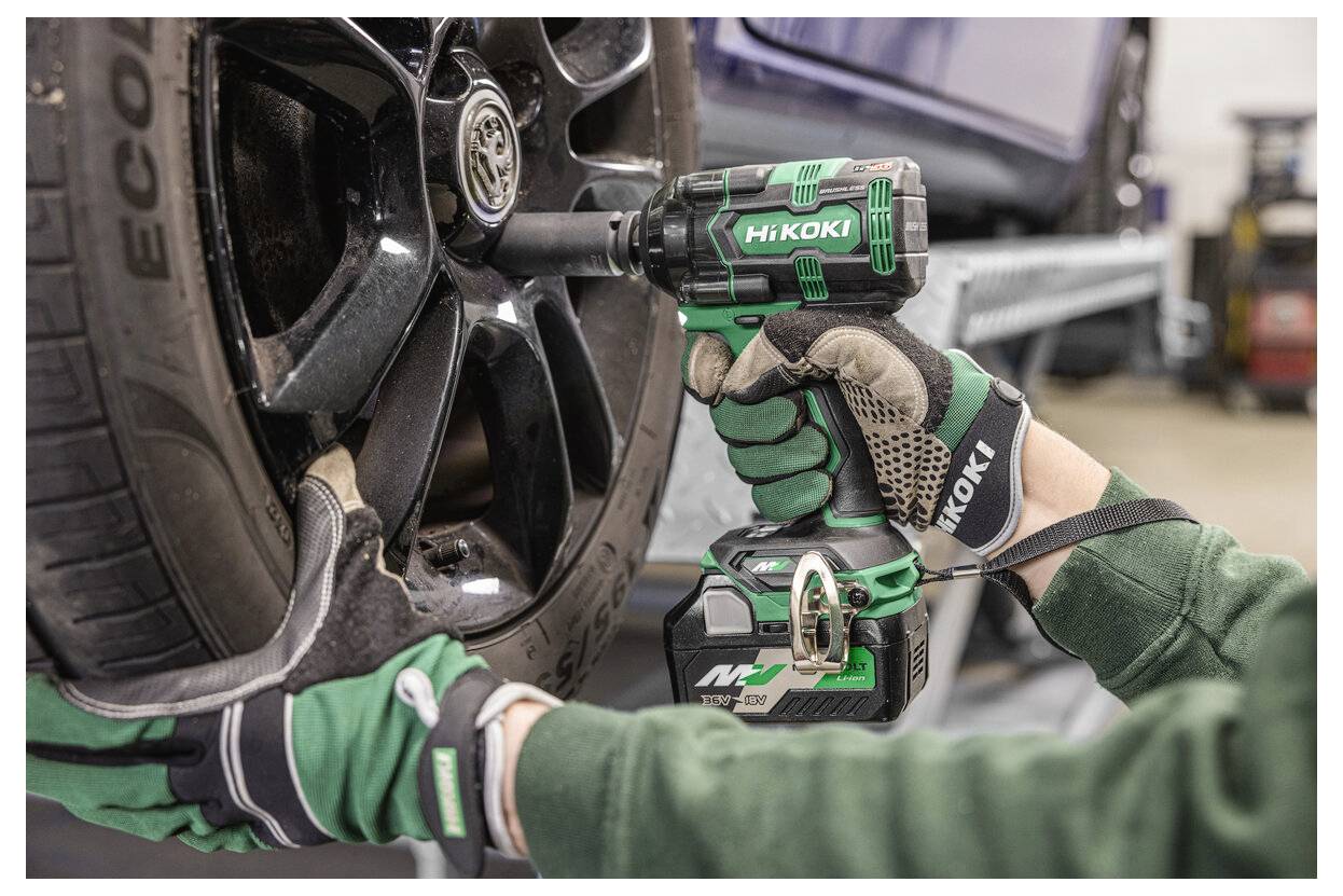 Eine Person mit Arbeitshandschuhen verwendet einen kabellosen Schlagschrauber, um eine Radmutter an einem Auto in einer Autowerkstatt zu befestigen.