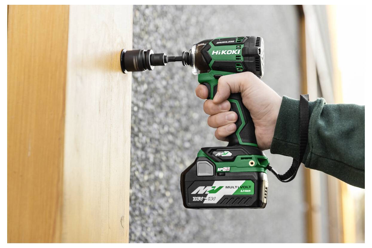 Eine Person, die einen grün-schwarzen kabellosen Bohrer verwendet, um ein Loch in eine Holzoberfläche zu bohren. Der Bohrer trägt die Aufschrift 'HiKOKI Multi Volt.'