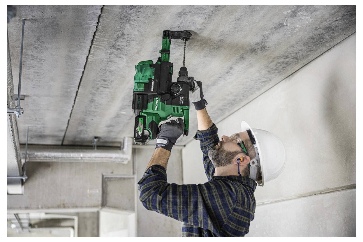 Ein Bauarbeiter in Sicherheitsausrüstung verwendet einen grünen Bohrhammer an einer Betondecke und konzentriert sich dabei auf Präzision und Stabilität.