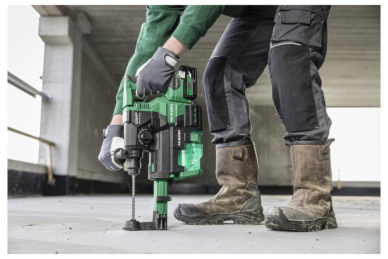 Eine Person mit Arbeitshandschuhen bedient eine grüne Bohrmaschine auf einem Betonboden und demonstriert dabei eine Bau- oder Renovierungsaktivität.