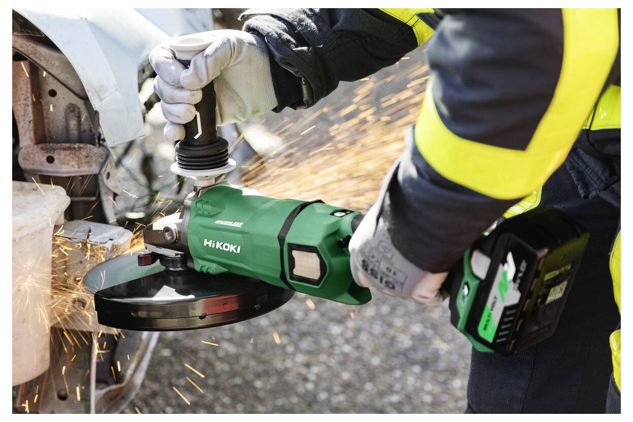 Eine Person mit Sicherheitsausrüstung verwendet ein grünes Werkzeug, um Metall an einem Fahrzeug zu schneiden, wobei Funken entstehen.