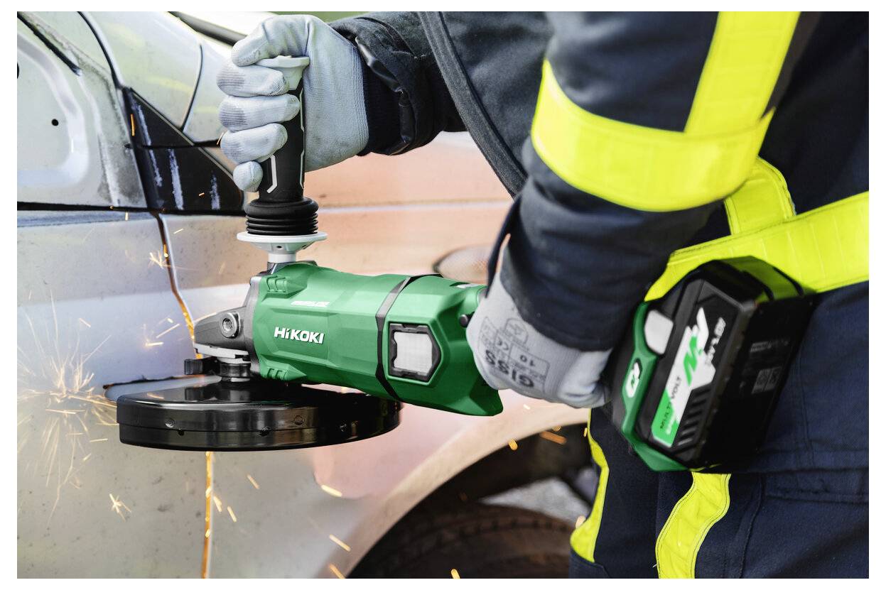 Eine Person in Schutzausrüstung verwendet einen grünen HiKOKI-Winkelschleifer zum Schneiden von Metall, wobei Funken entstehen. Der Fokus liegt auf dem Werkzeug und der Aktion.