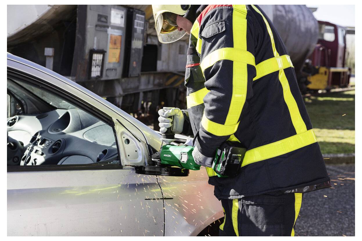 Ein Feuerwehrmann in Schutzausrüstung verwendet ein leistungsstarkes Werkzeug, um während einer Rettungsaktion eine Autotür aufzuschneiden, während Funken umherfliegen.