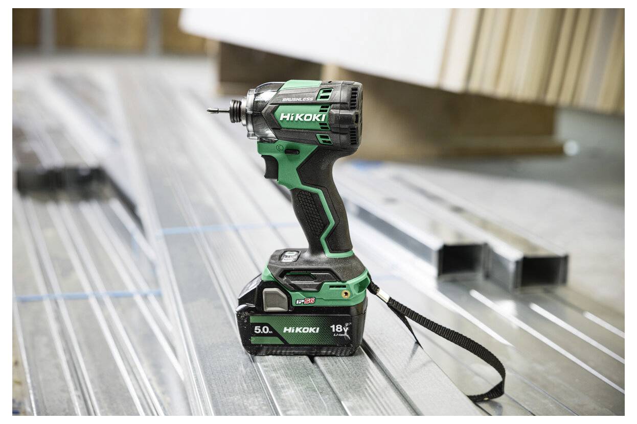 Eine grüne und schwarze Bohrmaschine der Marke HiKOKI liegt auf einer Metalloberfläche, umgeben von Stahlträgern, was auf eine Bauumgebung hindeutet.