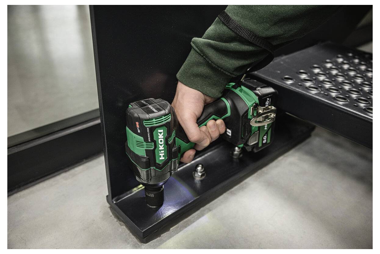 Eine Person verwendet einen grünen kabellosen Schlagschrauber mit der Bezeichnung 'HiKoki', um eine Schraube an einer Metallstruktur zu befestigen und damit seine Nützlichkeit im Baugewerbe zu demonstrieren.