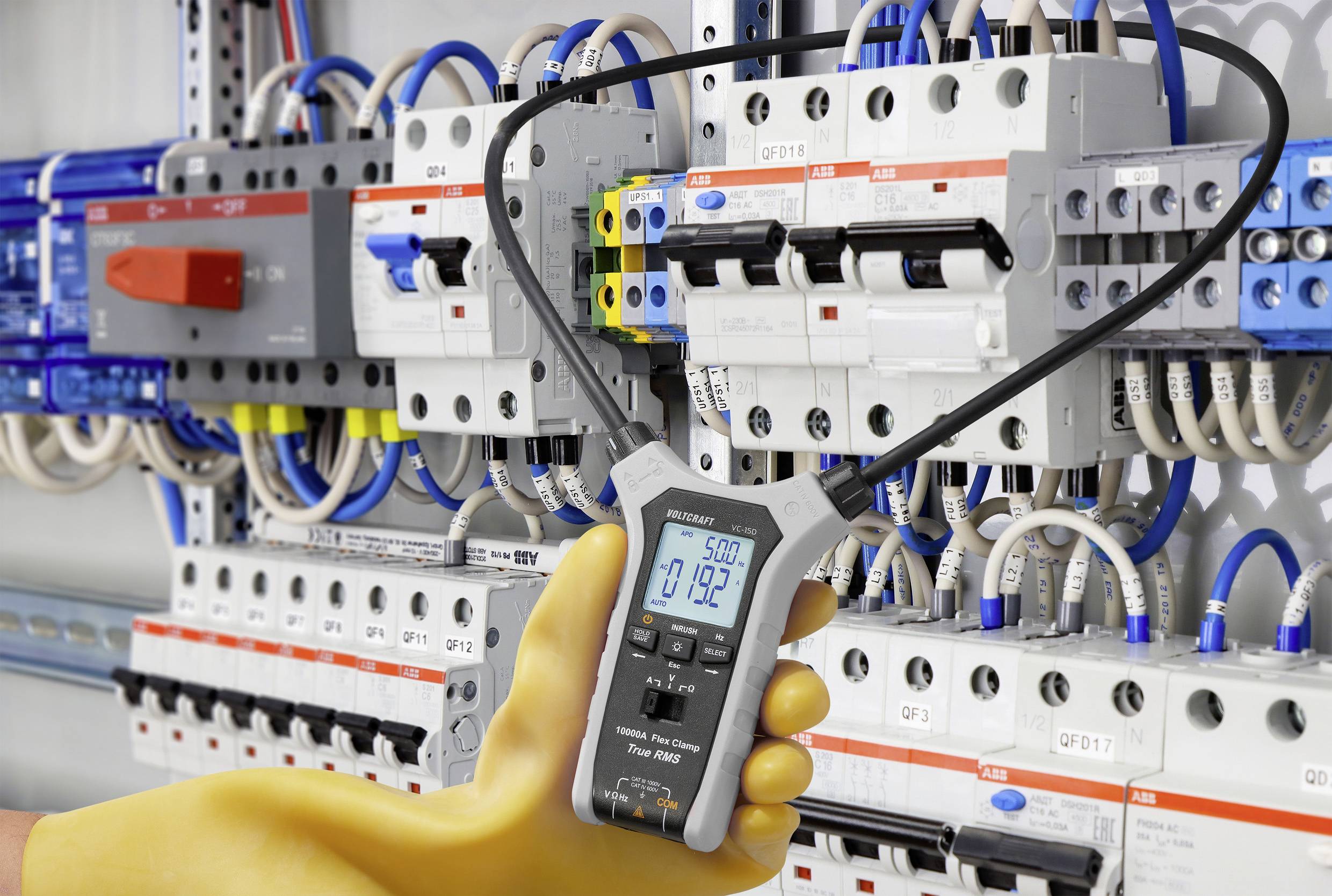 Eine Person mit isolierenden Handschuhen verwendet ein digitales Multimeter, um die Spannung an einer großen Elektrotafel mit Kabeln und Schaltern zu messen.