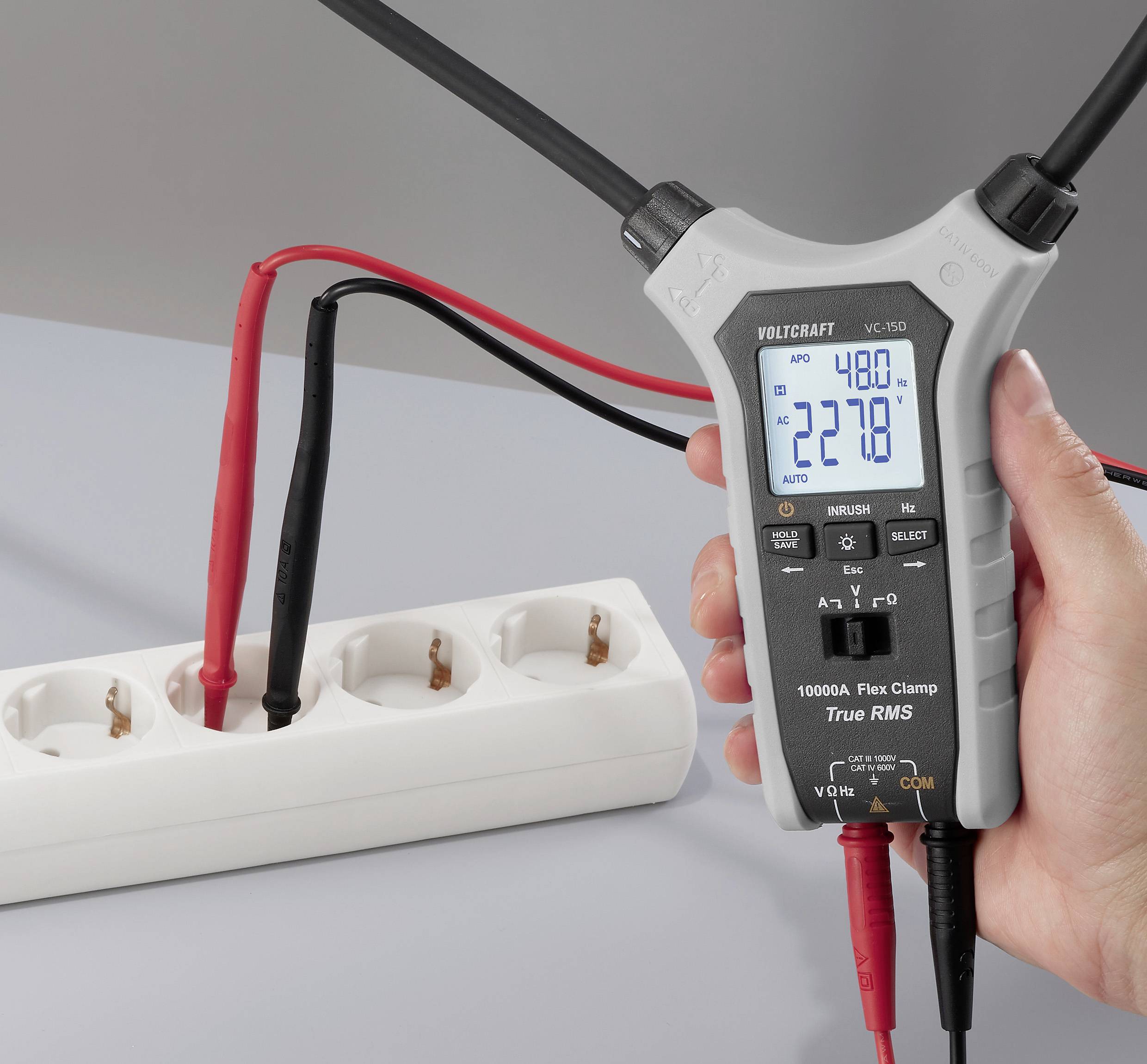 Ein digitales Zangenmessgerät zeigt Ablesungen von 48,0 und 227,8 an, das mit roten und schwarzen Messspitzen an einer Steckdosenleiste angeschlossen ist.