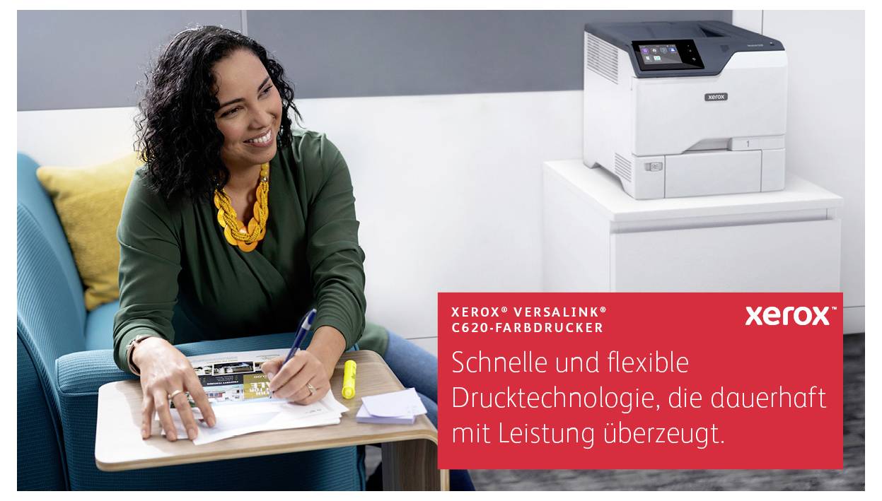 Eine Frau sitzt auf einem Stuhl und lächelt, während sie an einem Tisch schreibt. Neben ihr befindet sich ein Xerox-Farbdrucker.