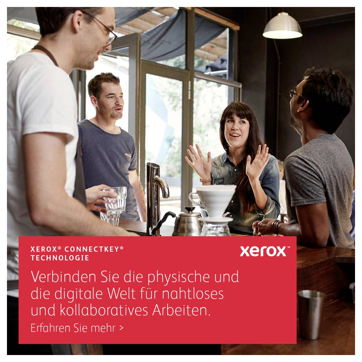 Eine Gruppe von vier Personen unterhält sich in einer Küche. Im Vordergrund ist ein Schild mit der Aufschrift 'Xerox ConnectKey Technologie'.