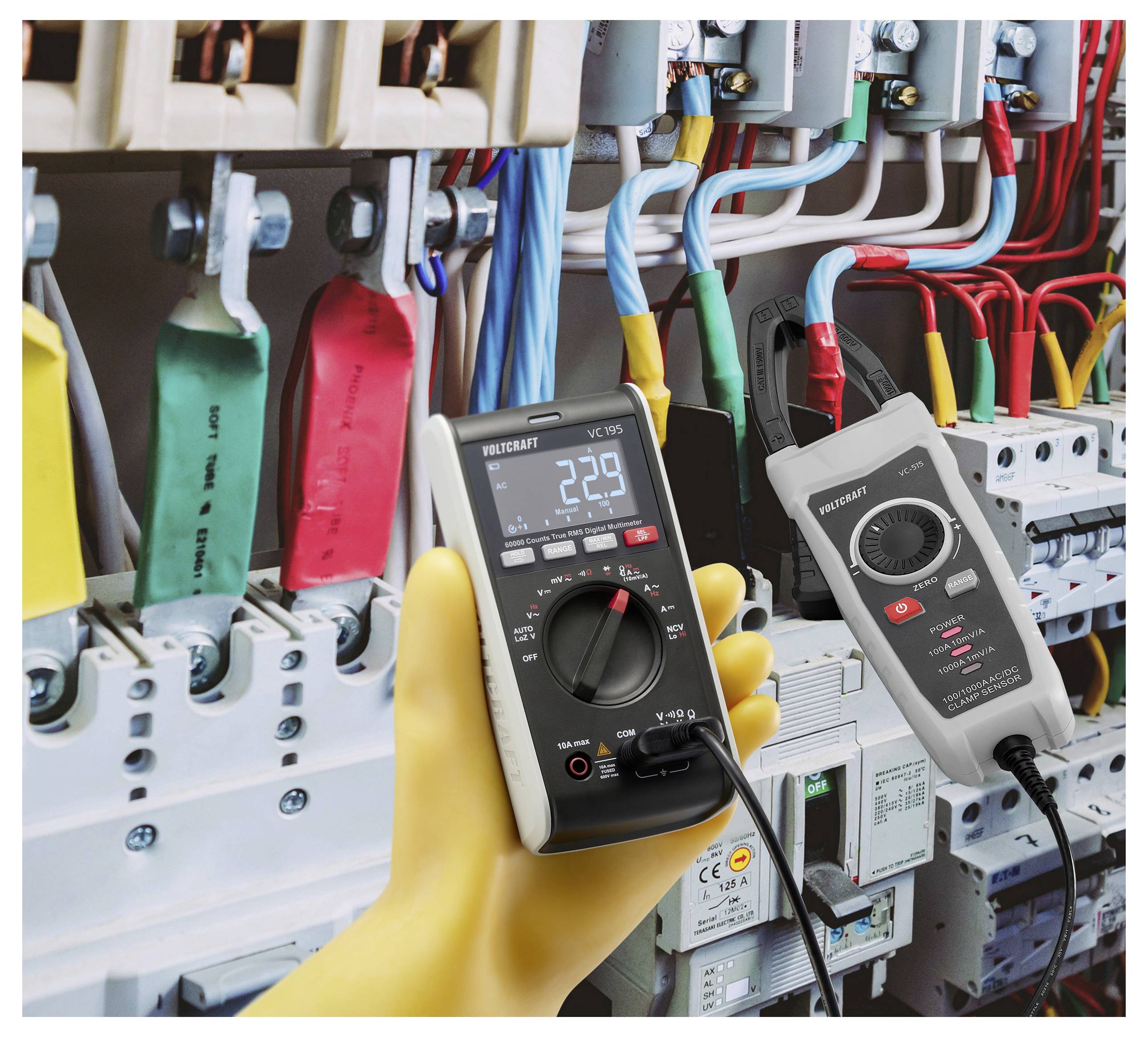 Eine Person, die ein digitales Multimeter mit angezeigten 22,9 Volt hält und elektrische Komponenten in einer Sicherungskasten mit verschiedenfarbigen Kabeln prüft.