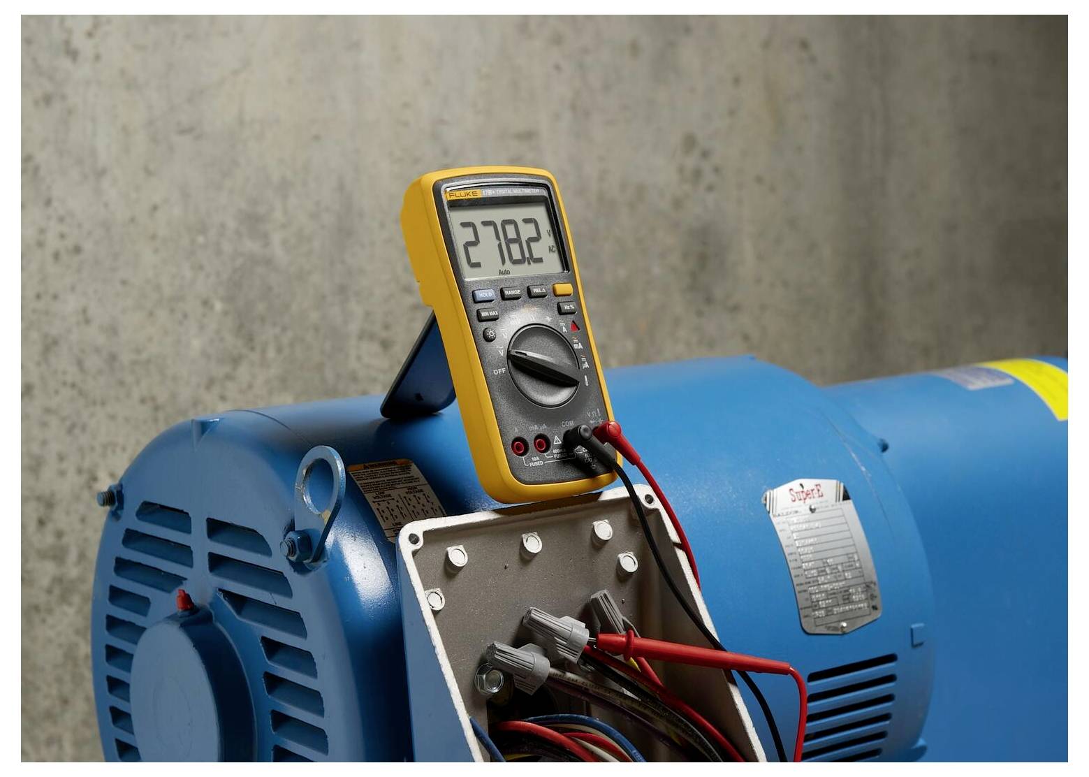 Ein digitales Multimeter zeigt '278,2' an, verbunden mit einem blauen Industriemotor, der die elektrische Spannung misst.