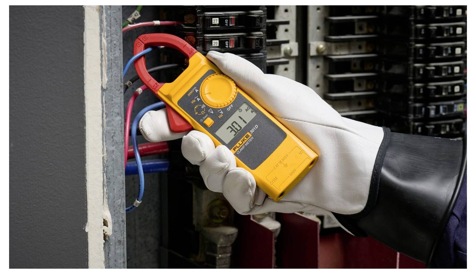 Eine Person mit Handschuhen verwendet eine gelbe Zangenstrommesszange an elektrischen Leitungen in einer Schalttafel und zeigt eine Ablesung von 201,2 an.