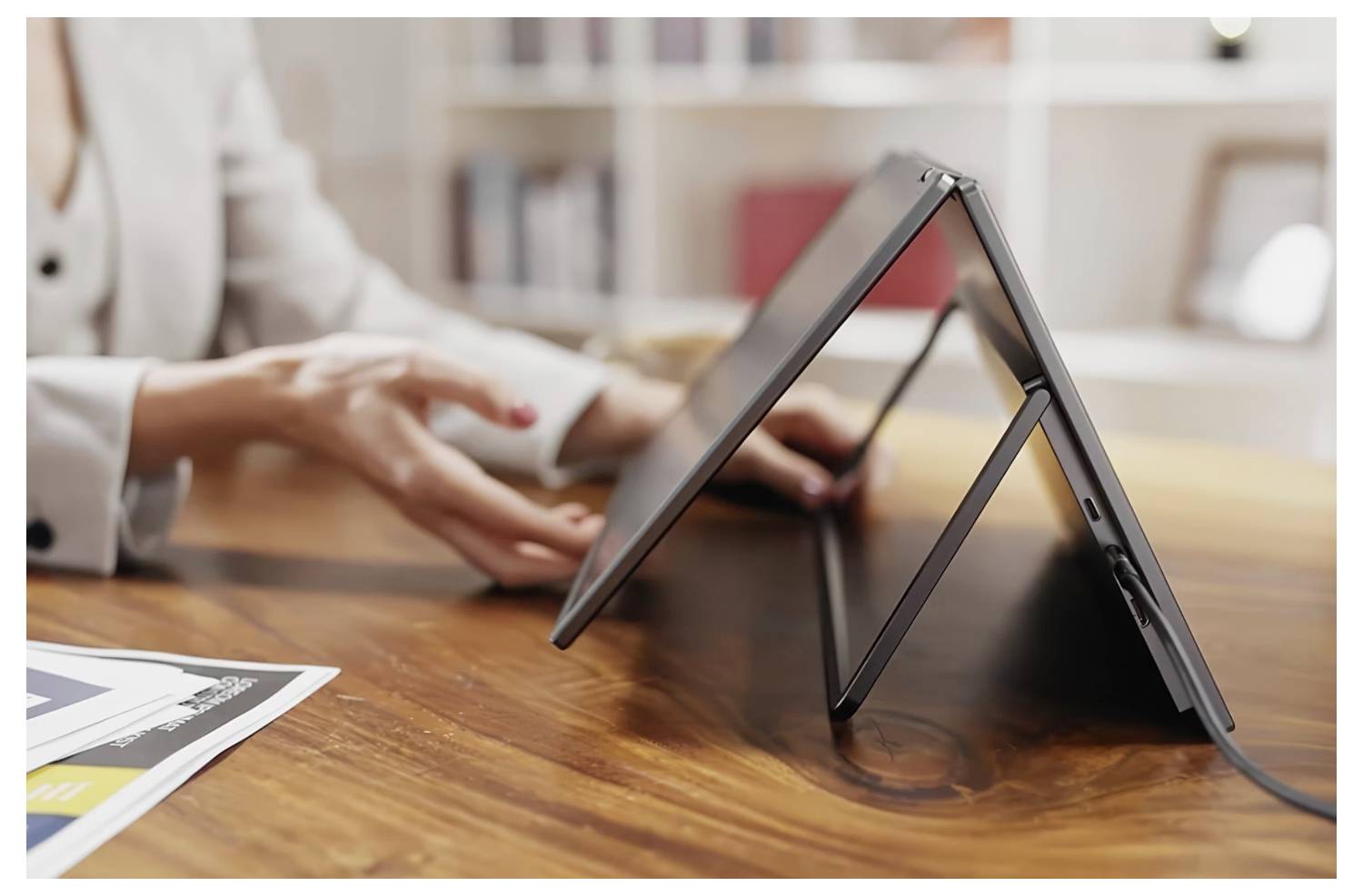 Eine Person demonstriert einen Laptop im Zeltmodus auf einem Holztisch und betont dessen flexibles Design für Benutzerfreundlichkeit in verschiedenen Umgebungen.