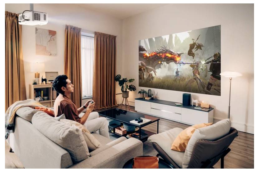 Eine Person sitzt auf einem Sofa und spielt ein Videospiel auf einer großen Projektionsleinwand, die eine Fantasie-Kampfszene in einem modernen Wohnzimmer zeigt.