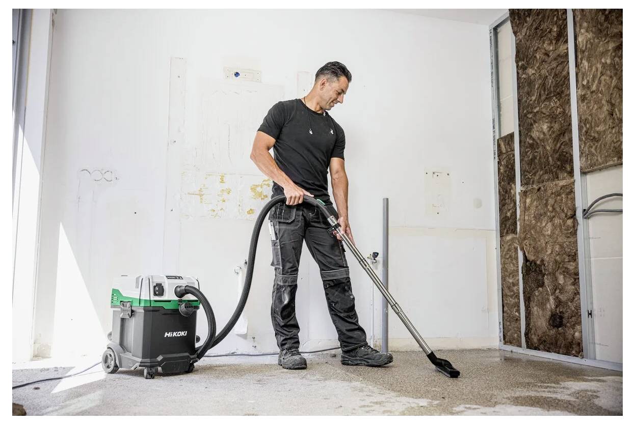 Eine Person, die einen Nass-Trockensauger auf einem Betonboden in einem teilweise renovierten Raum verwendet und damit Reinigungsausrüstung im Einsatz zeigt.