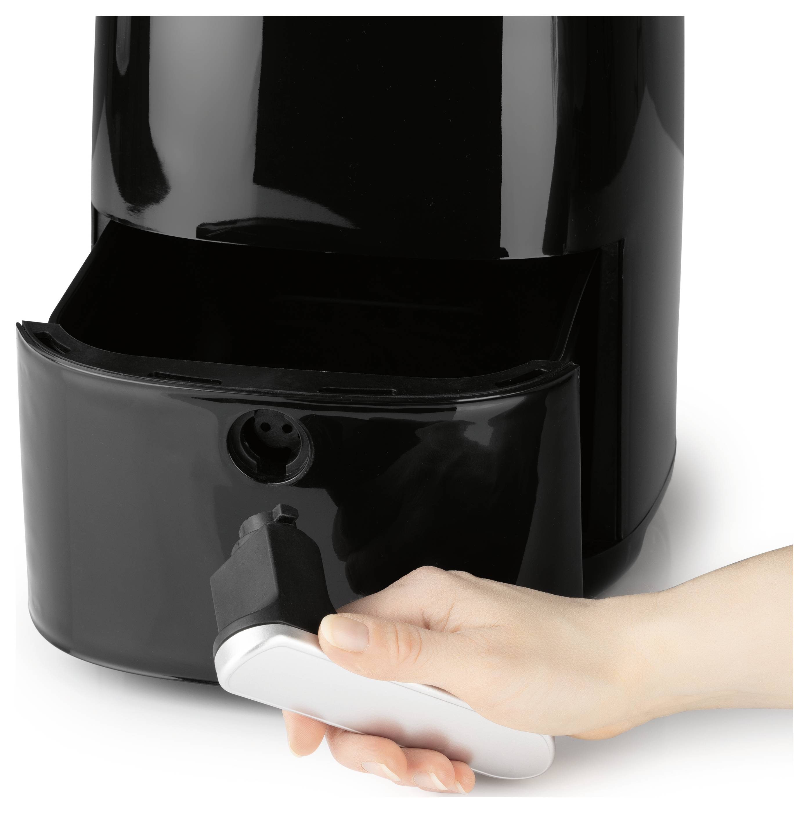 Eine Hand, die einen Löffel hält, entfernt Kaffeesatz aus der Schublade einer eleganten, schwarzen Kaffeemaschine.