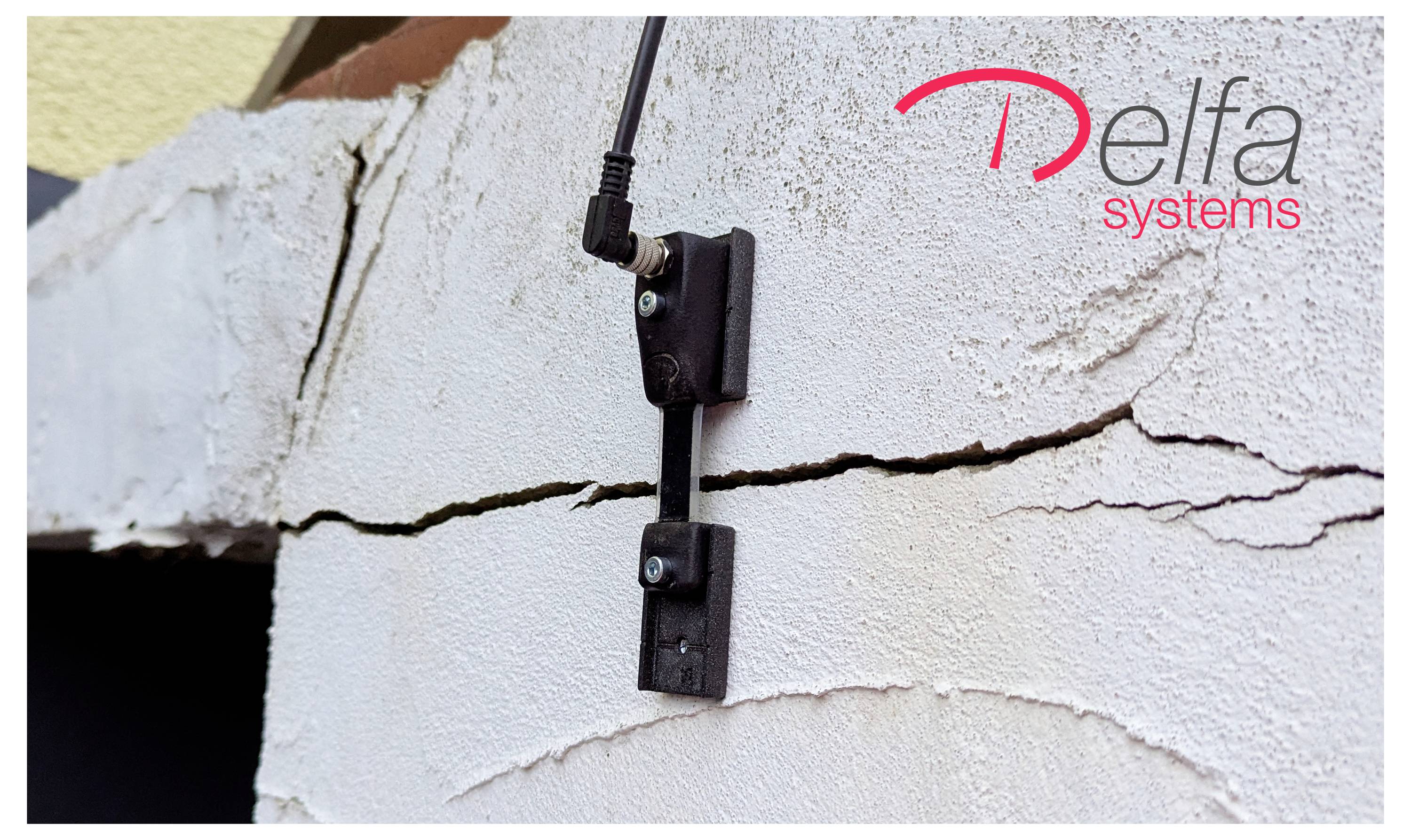 Ein an einer Wand befestigter elektronischer Sensor mit Kabel ist an einer gerissenen Oberfläche angebracht. Das Bild zeigt das Logo 'Delfa Systems' in der Ecke.