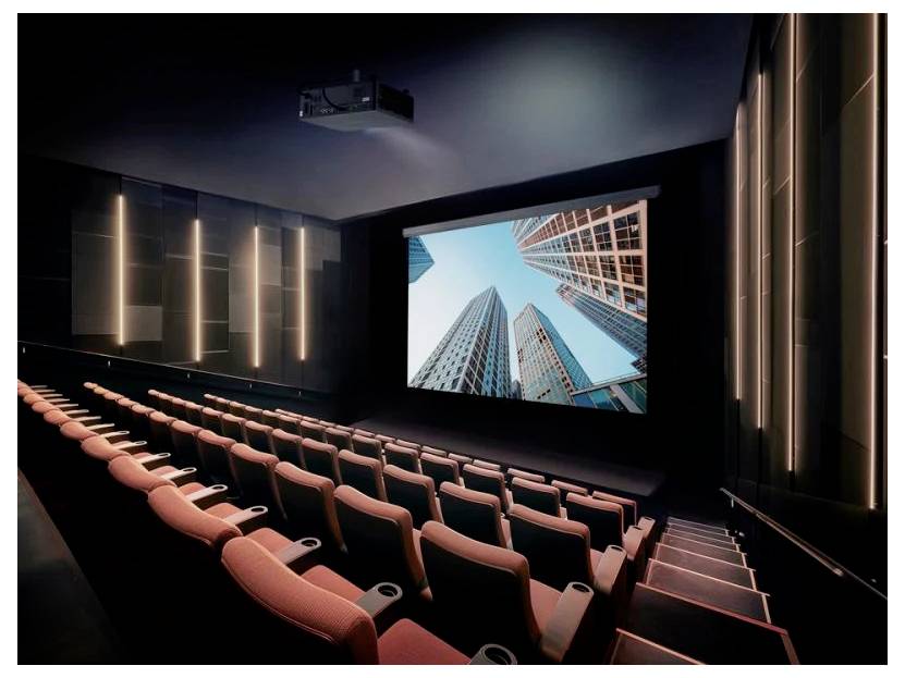 Innenraum eines modernen Kinos mit mehrstufigen Sitzreihen und einer großen Leinwand, auf der Wolkenkratzer zu sehen sind, was ein immersives Sehvergnügen schafft.