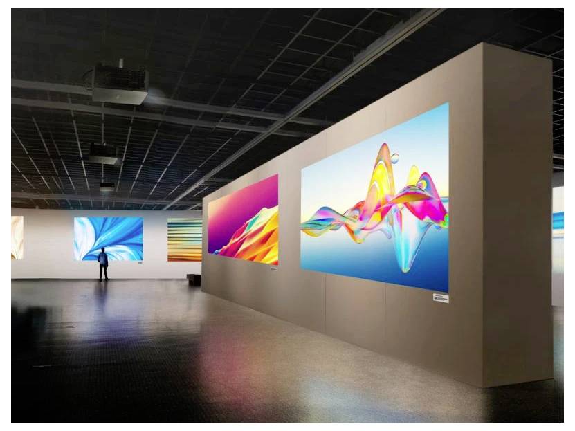 Eine Kunstgalerie mit großen, farbenfrohen abstrakten digitalen Kunstwerken an den Wänden. Eine Person steht und betrachtet eines der Werke.