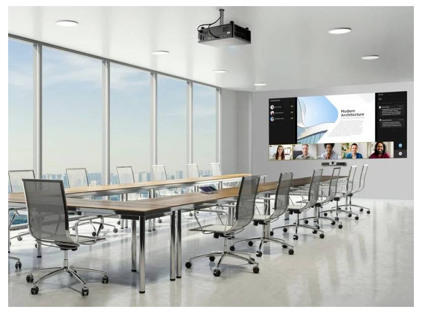 Ein moderner Konferenzraum mit einem großen Fenster und Ausblick, leere Stühle um einen langen Tisch herum. Ein Videoanruf wird auf einem Bildschirm angezeigt.