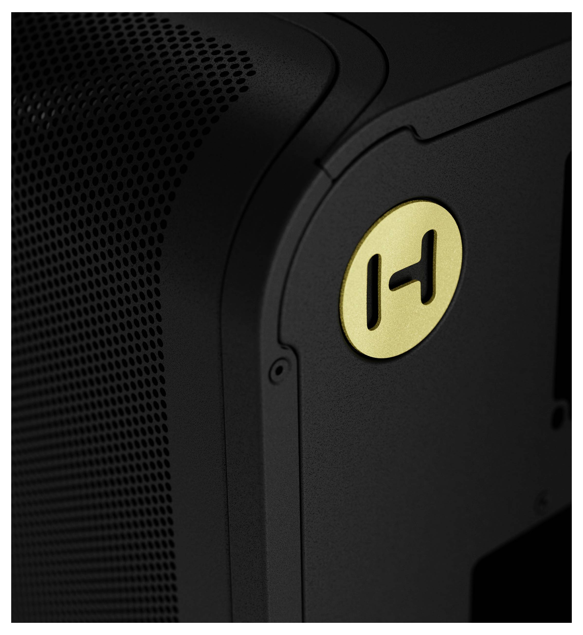Eine Nahaufnahme einer schwarzen Geräteecke mit perforierter Textur und einem kleinen runden goldenen Logo mit einem stilisierten 